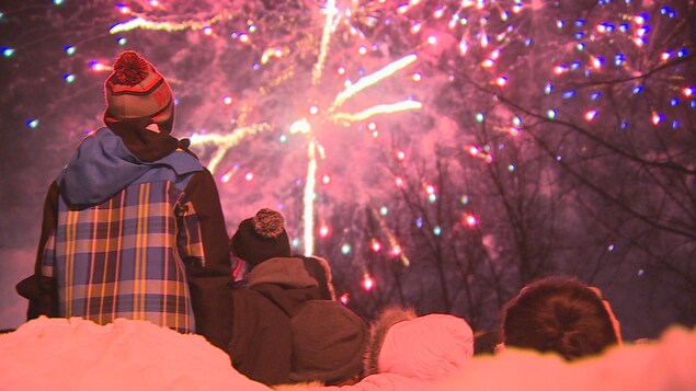 Des gens de dos regardent un feu d'artifice, en hiver.