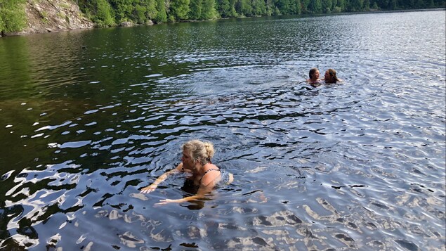 Trois personnes se baignent dans l'eau d'une rivière. 