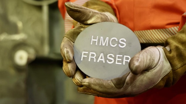 Un ouvrir tient dans ses mains un cercle métallique avec l'inscription HMCS Fraser.