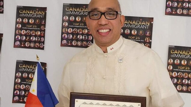 Hawak ni Edsel Mutia ang plake ng pagkilala at ang maliit na bandila ng Pilipinas.