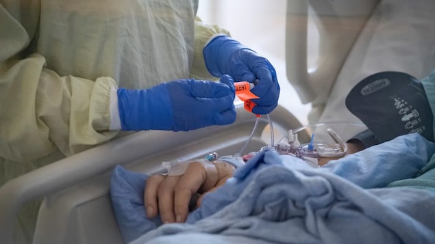 Une infirmière qui porte une jaquette jaune et des gants bleus est au chevet d'un patient. 