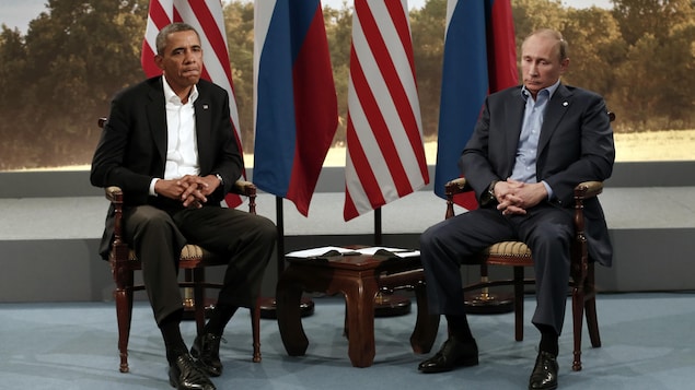 Barack Obama et Vladimir Poutine, assis devant des drapeaux russes et américains, regardent le sol, les mains croisées. Barack Obama et Vladimir Poutine, assis devant des drapeaux russes et américains, regardent le sol, les mains croisées.