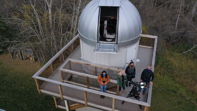 Des gens sur la plateforme de l'observatoire Hesje scrutent le ciel avec un télescope.