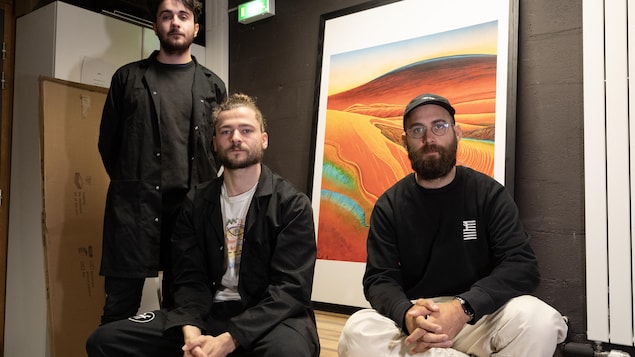 Trois hommes prennent la pose devant une oeuvre d'art inspirée d'un volcan. 