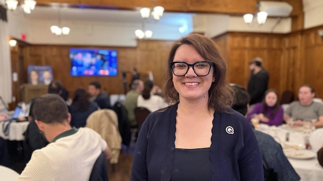 Odette Lavigne pose dans une salle où des militants sont rassemblés autour de tables.