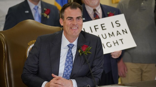 Kevin Stitt, une rose à la boutonnière, arbore un large sourire devant une pancarte disant : « La vie est un droit de la personne ».
