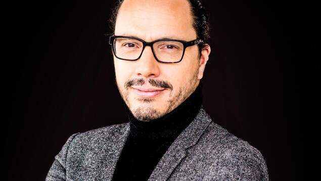 L'homme a les cheveux attachés, des lunettes, et il regarde la caméra. L'homme a les cheveux attachés, des lunettes, et il regarde la caméra.