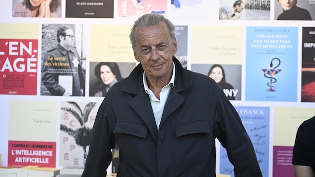 Un homme pose devant des couvertures de livres. 
