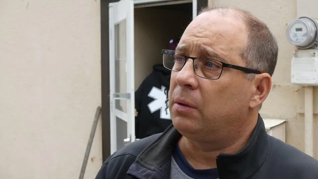 Un homme ayant l'air épuisé parle avec tristesse à un journaliste hors cadre. Il se tient devant le mur d'un bâtiment. Un homme ayant l'air épuisé parle avec tristesse à un journaliste hors cadre. Il se tient devant le mur d'un bâtiment.