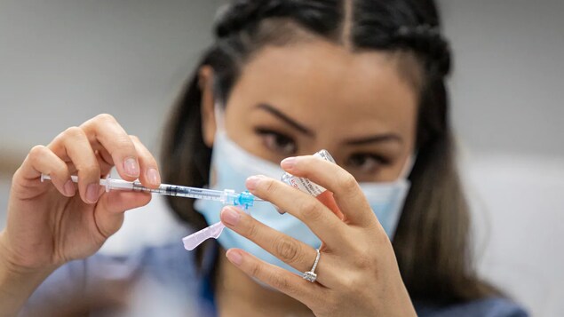 Isang health-care worker na may hawak na injection at vial.