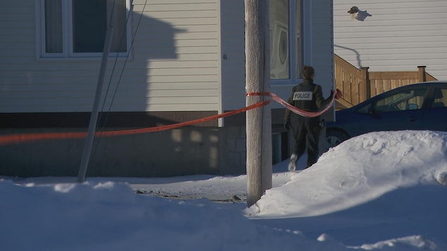 Un agent de police déroule un ruban devant une maison.