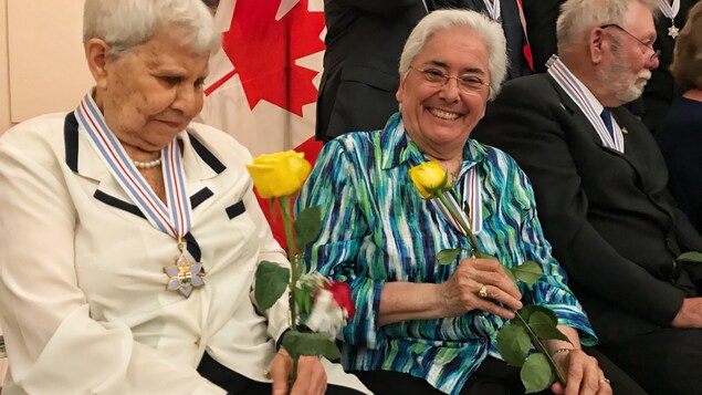 Plusieurs personnes décorées d'une médaille, et deux femmes tenant des roses jaunes. Plusieurs personnes décorées d'une médaille, et deux femmes tenant des roses jaunes.