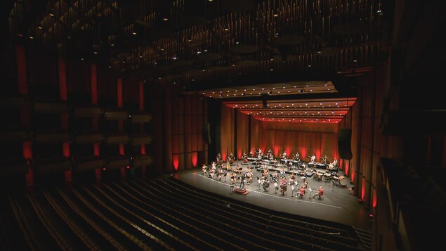 Des musiciens et musiciennes sur la scène d'une salle de spectacle vide.