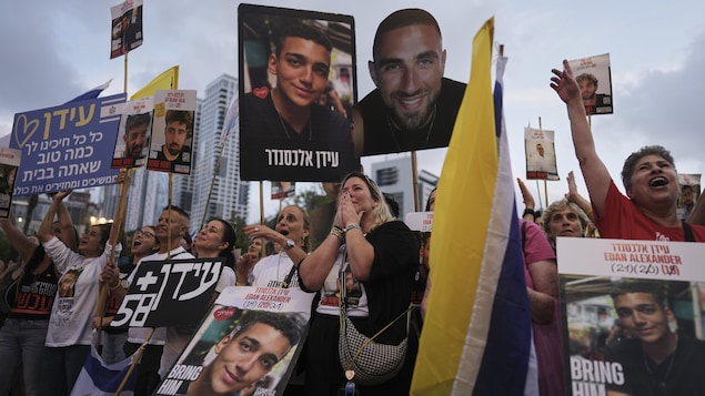 Des personnes émues dans la rue brandissent le drapeau israélien et des affiches arborant le portrait d'Edan Alexander.