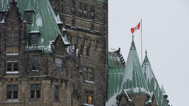 Les pignons du bâtiment de la confédération et au loin, le drapeau du Canada au vent.