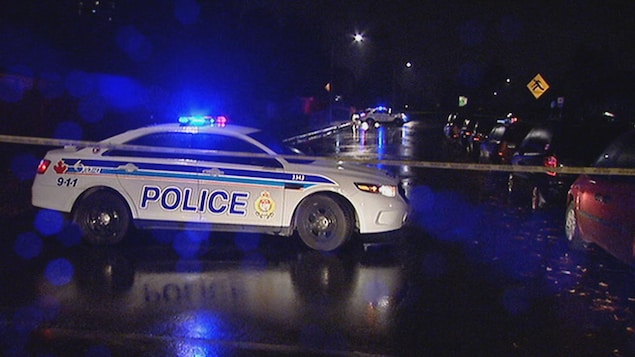 Une voiture du Service de police d'Ottawa en pleine nuit, à l'intérieur d'un périmètre de sécurité. Ses gyrophares sont allumés.