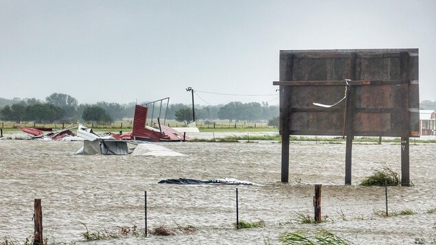 Des débris, vraisemblablement des ruines d'habitations, sont transportés dans les champs par l'eau et le vent, devant un panneau de signalisation. Des débris, vraisemblablement des ruines d'habitations, sont transportés dans les champs par l'eau et le vent, devant un panneau de signalisation.