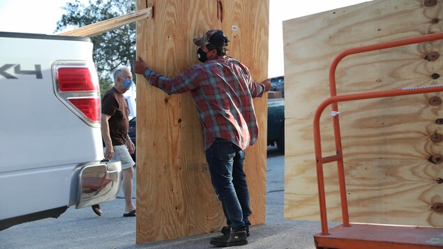 Un homme se prépare à charger un morceau de plywood bien plus grand que lui dans son camion.
