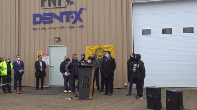 Des personnes sont derrière un podium devant une usine.