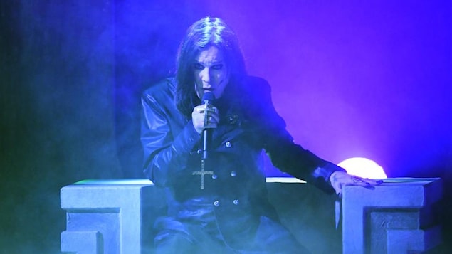 Ozzy Osbourne, sur scène, porte un micro avec une croix.