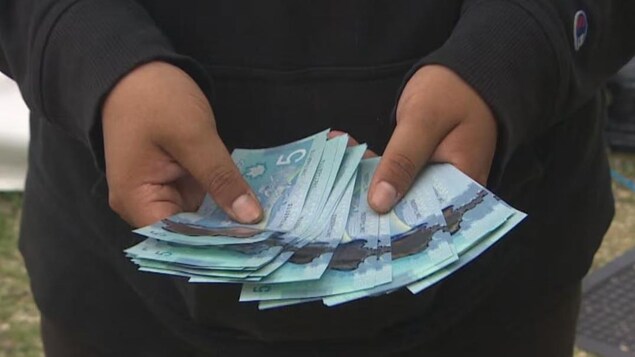 Une main tient des billets de 5 $ canadiens.