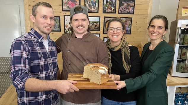 Quatre personnes tiennent un pain sur une planche.