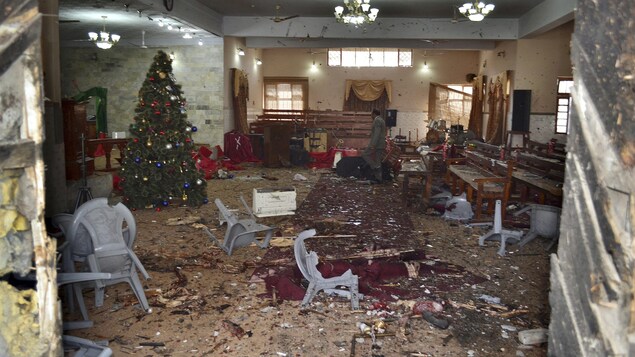 Photo de l'intérieur de l'église où l'on voit plusieurs débris au sol et des trous de balles dans les murs. Un arbre de Noël est toujours debout. Photo de l'intérieur de l'église où l'on voit plusieurs débris au sol et des trous de balles dans les murs. Un arbre de Noël est toujours debout.
