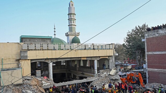 Une mosquée démolie par une explosion avec une foule à proximité.