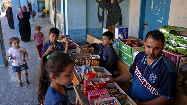 Un homme se trouve derrière une table où se trouvent des bonbons. Des enfants l'entourent.