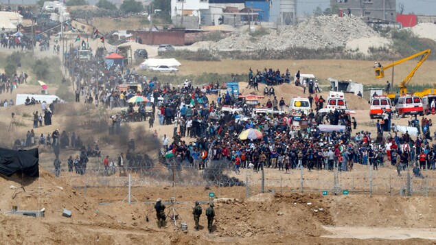 Des centaines de Palestiniens manifestent près d'une clôture protégée par trois soldats israéliens. 