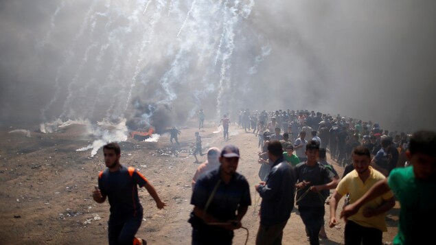 Des manifestants palestiniens se sauvent des gaz lacrymogènes tirés par les troupes israéliennes lors d'une manifestation contre le transfert de l'ambassade américaine à Jérusalem, à la frontière entre Israël et Gaza le 14 mai 2018.