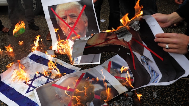Des manifestants brûlent une photo de Donald Trump de même que des drapeaux américains et israéliens. Des manifestants brûlent une photo de Donald Trump de même que des drapeaux américains et israéliens.