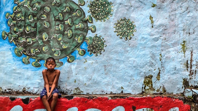 Un jeune garçon assis devant une murale représentant le coronavirus.