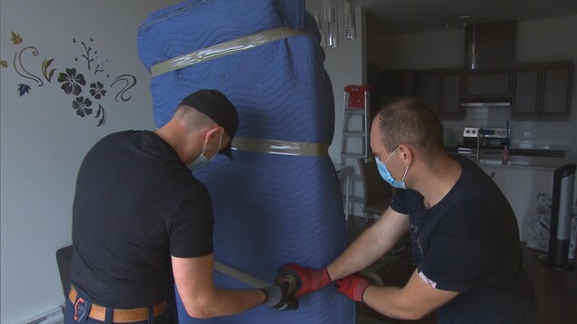 Des déménageurs recouvrent un meuble d'une enveloppe protectrice.
