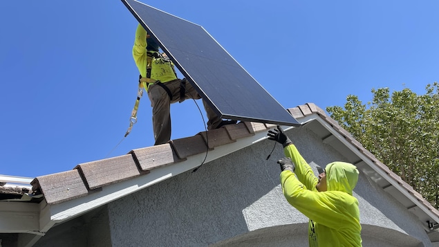 Deux ouvriers installent des panneaux solaires sur le toit d'une maisons.