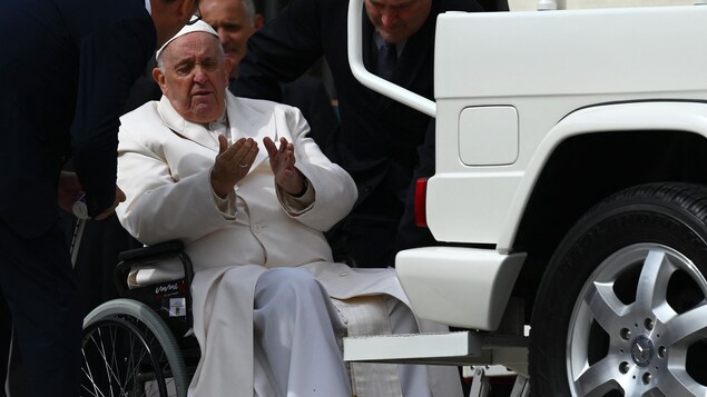 Le pape François est assis dans un fauteuil roulant près de la papemobile.