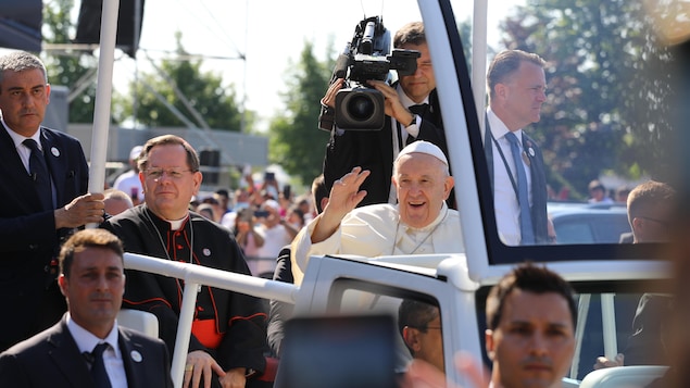 Les deux hommes souriant assis dans la papemobile. Le pape envoie la main à la foule.