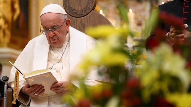 Le pape, assis, lit un passage liturgique.