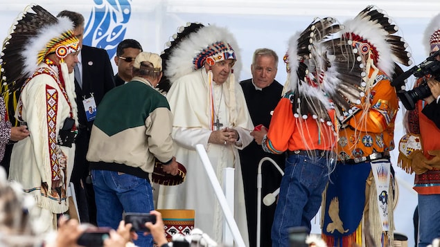 Le pape François est debout avec une coiffe sur la tête. 
