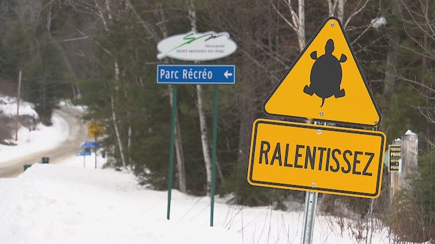 Une pancarte jaune où l'on peut voir une image de tortue et le mot «ralentissez» devant un écriteau annonçant l'entrée du Parc récréotouristique. 