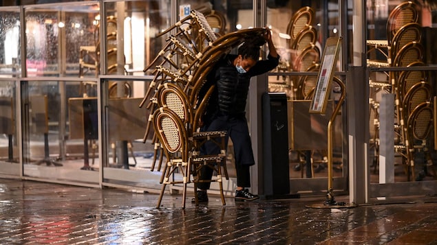 Une femme portant une pile de chaises sur une terrasse.