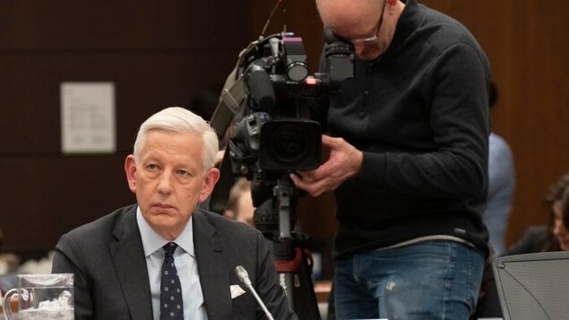 A man is sitting; a cameraman stands behind him.