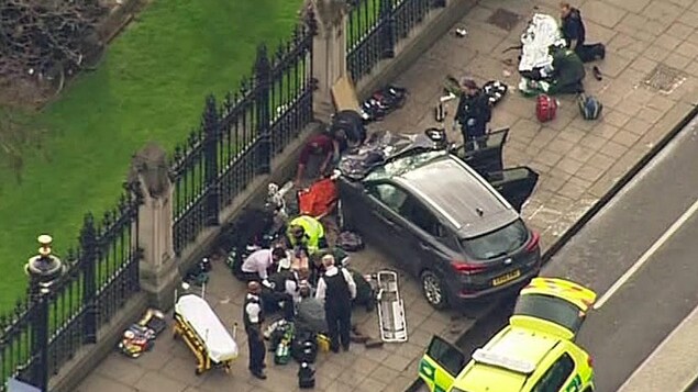 Cette image extraite d'une vidéo montre des policiers et des ambulanciers prêtant assistance à des blessés près de l'endroit où un véhicule utilitaire sport a percuté la grille qui ceinture le palais de Westminster. 