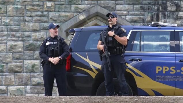 Des agents armés debout près d'un véhicule du Service de protection parlementaire.