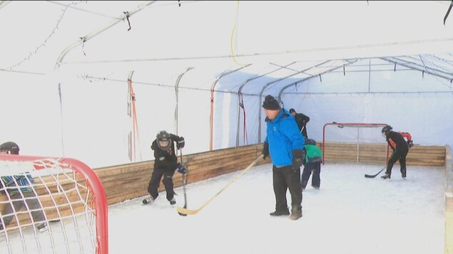 Une famille joue au hockey sur une patinoire privée, installée sous un abri tempo.