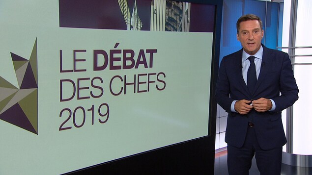 Patrice Roy à côté d'un écran où l'on peut lire « Le débat des chefs 2019 ».