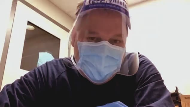 Un infirmier vêtu d'équipement de protection individuelle regardant la caméra.