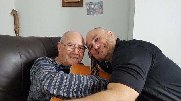 Earl Leblanc et Patrick Truner se font une accolade autour d'une guitare.