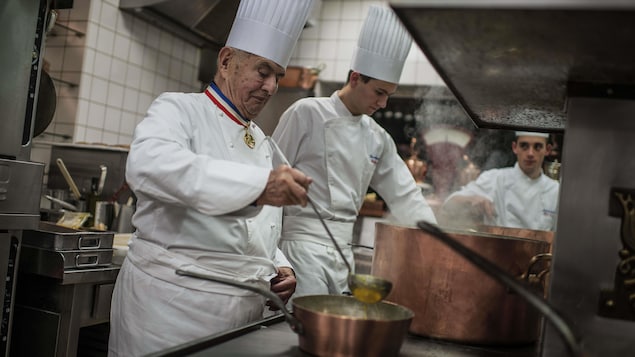 Le chef Paul Bocuse tient une grande louche dans sa main droite au-dessus d'une casserole. Le chef Paul Bocuse tient une grande louche dans sa main droite au-dessus d'une casserole.
