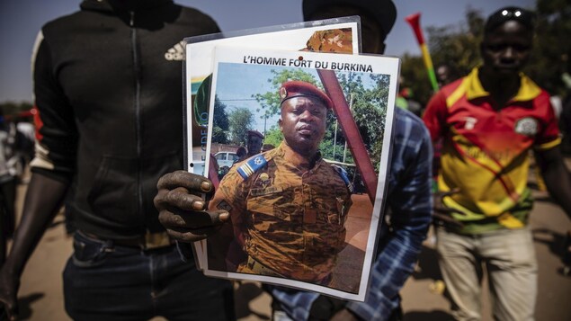 Un homme montre une affiche d'un homme en uniforme sur laquelle on peut lire : « L'homme fort du Burkina ».